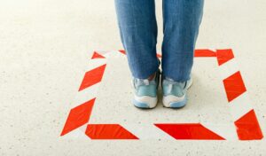 Red striped line sign for keeping social distance. Woman standing behind a warning line during covid 19 coronavirus quarantine. 