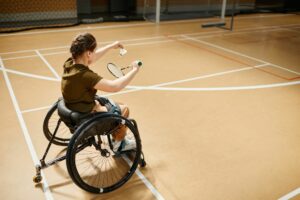 Portrait en plongée d'une jeune femme en fauteuil roulant jouant au badminton lors d'un entraînement sportif sur un terrain couvert.